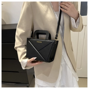 Detail of black crossbody bag featuring geometric triangle stitching and gold fashion text