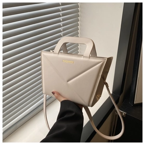 Close-up of beige handbag featuring geometric V-fold design and gold fashion text