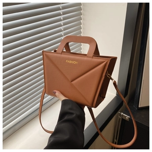 Close-up of brown PU leather bag with geometric folds and golden fashion text detail