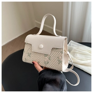 Detail of cream crossbody bag with green floral embroidery and round buckle closure