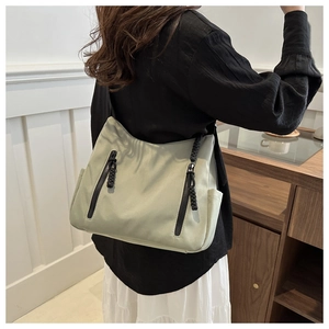 Détail du sac cabas vert clair avec poche latérale et fermetures éclair noires sur la bandoulière