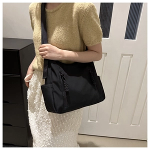 Détail d'un grand sac à bandoulière en nylon noir avec cordons tressés et poche latérale