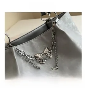 Close-up of silver tote bag featuring double metal chains and a bow pendant detail