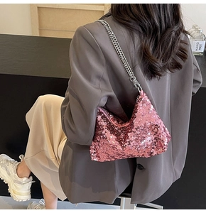 Detail of pink sequin hobo bag with silver chain strap worn by a model in modern setting