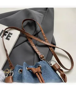 Top view of blue denim bucket bag featuring brown leather trim and adjustable strap detail