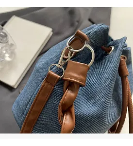 Detail of denim bucket bag showing brown braided leather handle and silver metal hardware