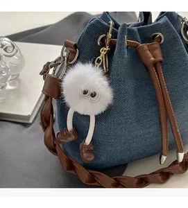 Detail of denim bucket bag with brown woven leather strap and cute plush monster charm