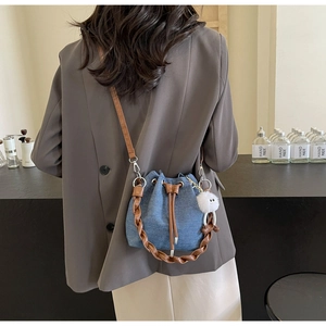 Detailed view of blue denim bucket bag with brown woven handle and plush charm on model