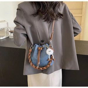 Close-up of denim bucket bag with woven leather handle and plush charm in a cafe setting