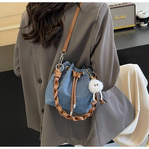 Detail of blue denim bucket bag with brown drawstring and plush doll pendant on model