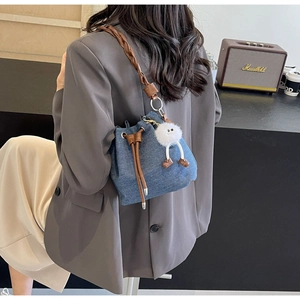 Detail of blue denim bucket bag with leather drawstring and plush monster charm