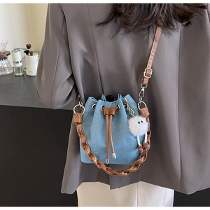 Detail of denim bucket bag with brown leather trim, woven handle and plush charm