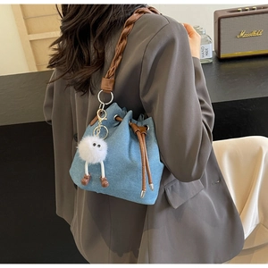 Detail of denim bucket bag featuring brown braided strap and plush monster charm