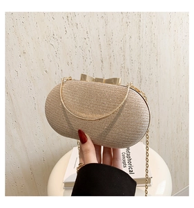 Detail of glittery gold oval evening clutch with bow clasp and delicate chain strap