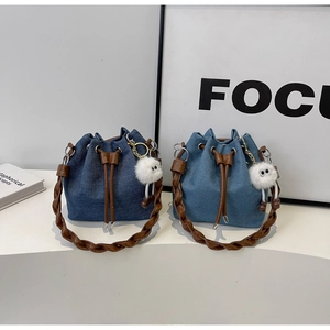 Detail of denim drawstring bucket bags featuring braided handles and plush eye charms