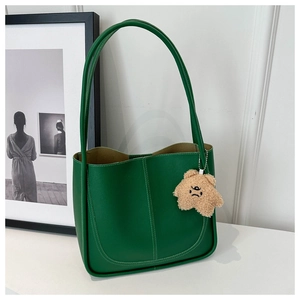 Dettaglio della borsa tote in pelle verde con cuciture bianche a contrasto e charm orso