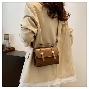 Brown vintage leather handbag with gold buckles shown on a beige blazer model outfit