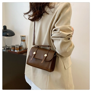 Detail of vintage dark brown leather crossbody bag paired with an elegant white blazer