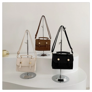Detail view of stylish square handbags in beige, brown, and black with gold metal buckles