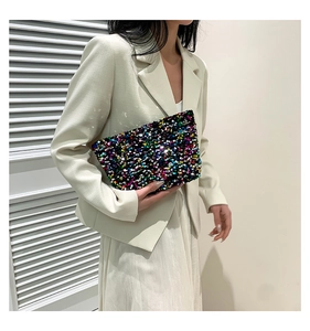 Chic handheld sequin pouch held by a model in a blazer against a minimal background