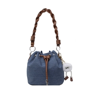 Blue denim bucket bag with brown woven leather handle and white plush charm on white background