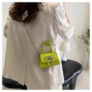 Detail of neon green mini handbag with rhinestone bow and silver chain strap for women