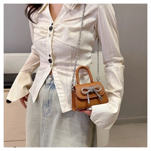 Close-up of brown mini handbag with silver rhinestone bow and metal chain strap
