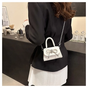 Close-up of white mini crossbody bag featuring a rhinestone bow and silver chain strap