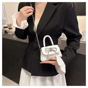 Close-up of a white mini handbag with a sparkling rhinestone bow and silver chain strap