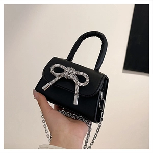 Detail of a black mini handbag featuring a shiny silver rhinestone bow and chain strap