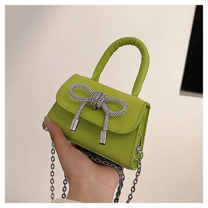 Detail of neon green mini handbag featuring a silver rhinestone bow and metal chain