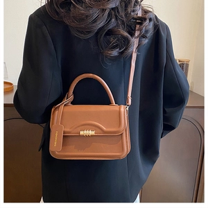 Detail of a brown leather crossbody bag featuring a gold rotating clasp and fashion tag