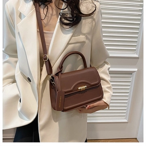 Detail of dark brown leather square bag with golden cylindrical metal clasp and strap
