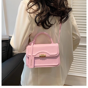 Detail of pink crossbody bag with gold cylindrical lock worn over a light blazer