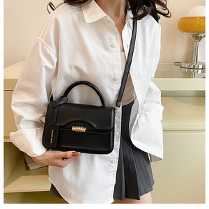 Detail of minimalist black handbag showing gold twist lock and smooth leather texture