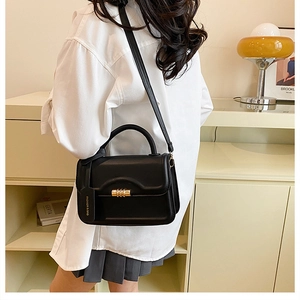 Detail of a black PU leather crossbody bag with a gold cylindrical turn lock and tag