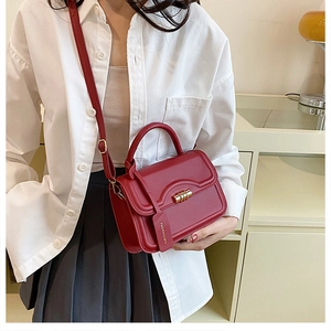 Red crossbody bag with gold buckle and fashion tag worn on a casual white shirt