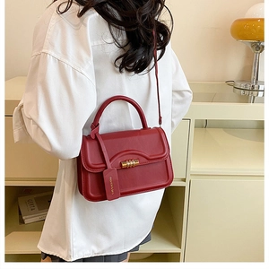 Red leather handbag with gold buckle shown worn by a model in a minimalist setting