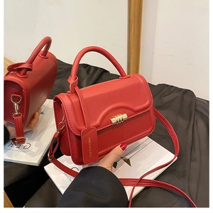 Detail of red matte faux leather handbag with gold twist lock and fashion tag