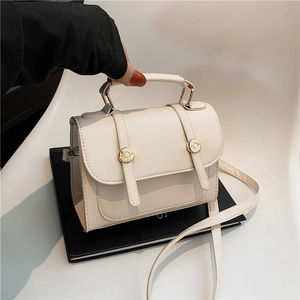Retro cream faux leather crossbody bag with gold buckle on black book display