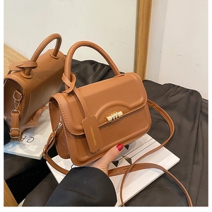 Detail of caramel brown PU leather handbag featuring gold metal clasp and hangtag