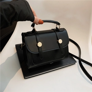 Retro black leather handbag with gold metal accents and top handle shown in a studio setting