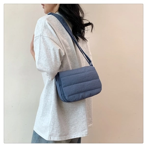 Detail view of blue quilted crossbody bag featuring soft down-like texture and wide strap