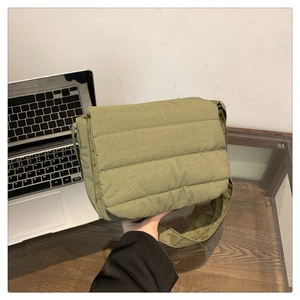 Detail of olive green quilted shoulder bag with wide strap on a wooden office desk