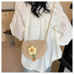 Detailed view of beige woven crossbody saddle bag with yellow knitted flower on a model