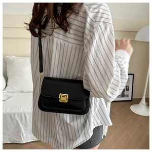 Detail of minimalist black leather square bag with gold buckle on shoulder