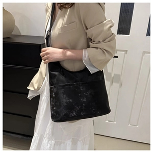 Détail du sac cabas noir texturé avec deux poches avant sur fond de blazer beige