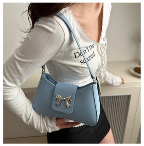 Close-up of light blue underarm bag featuring a metallic silver bow on the front flap