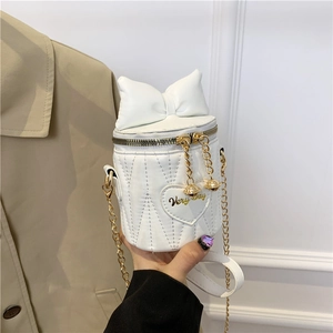 Weiße gesteppte Eimertasche mit Schleifendetail und Goldkette auf beigem Mantel