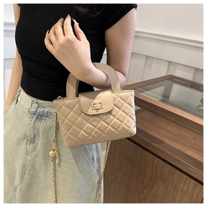 Détail d'un sac à main beige matelassé avec fermoir doré rotatif et bandoulière chaîne